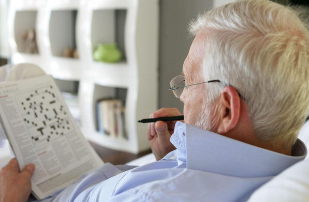 A reclining senior muses over a crossword in a physical newspaper as a relaxing solo activity in their senior living home