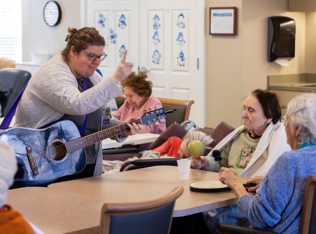 seniors in memory care play instruments with a carer holding a guitar