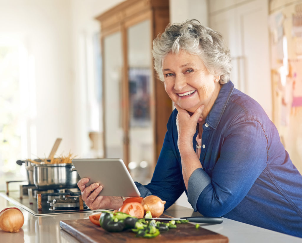 Older woman in kitchen using tablet while cooking