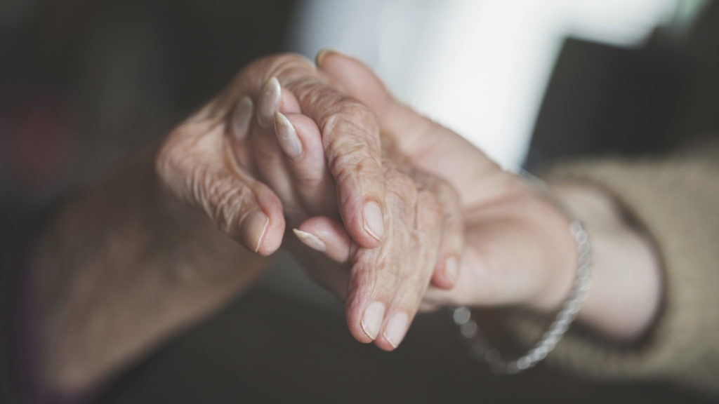 Close up of senior hand being held by younger hand. 