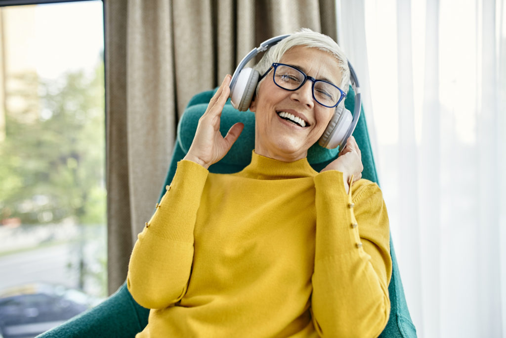 Senior woman sitting in armchair, listening music with headphones