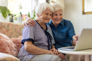 Adult daughter teaching her elderly mother to use laptop
