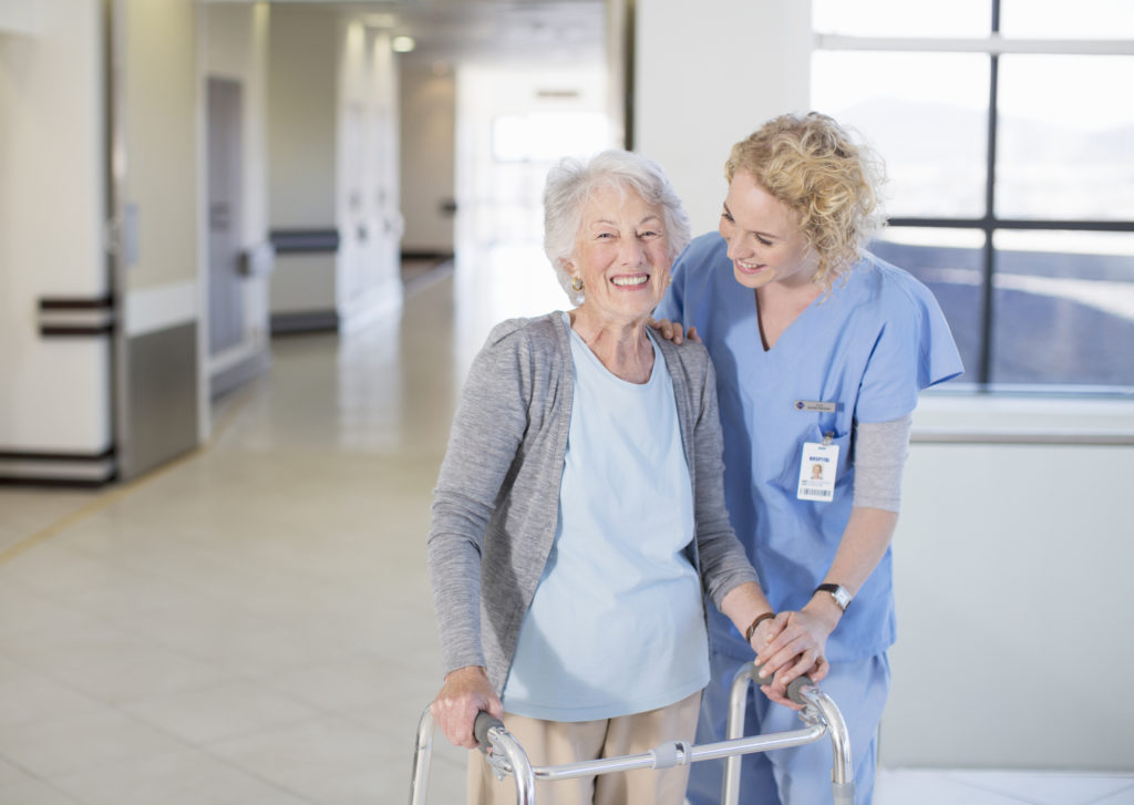 Nurse helping senior patient with walker in hospital corridor