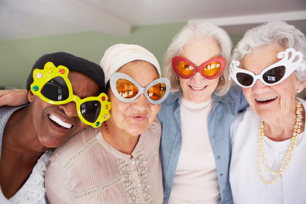 A group of elderly woman wearing funky sunglasses while standing in a nursing home