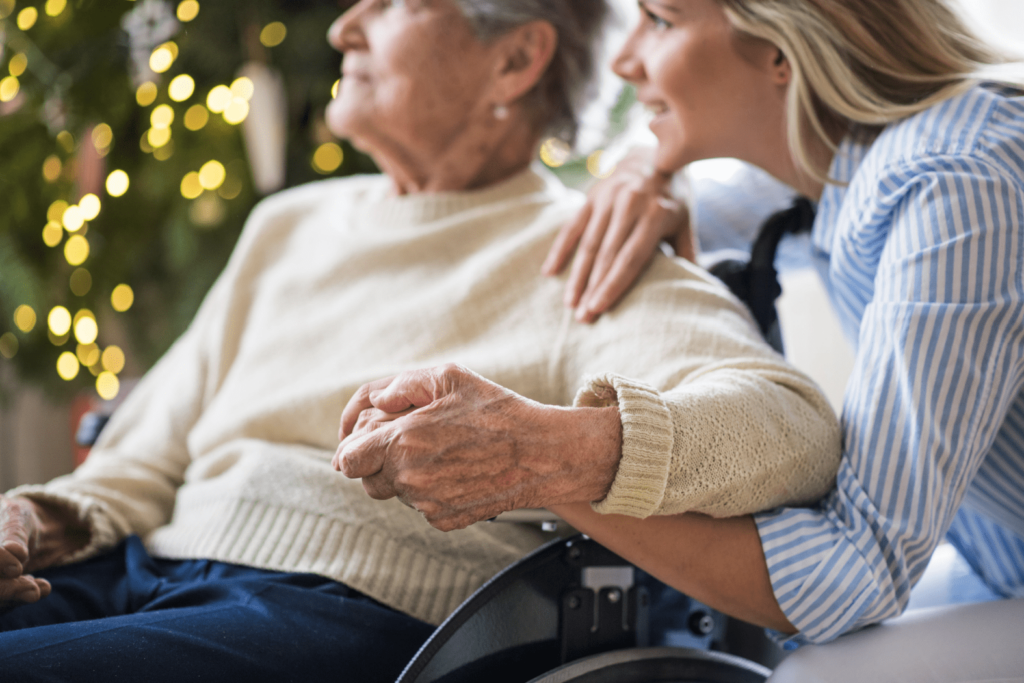 A woman holding her mothers hand as they look at something in the distance with a christmas tree in the background