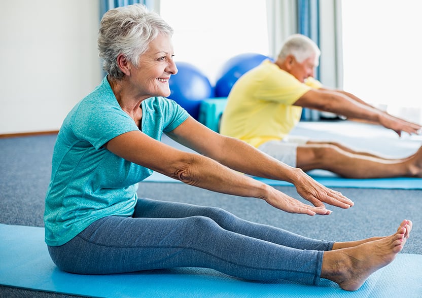mature woman and man sitting on yoga mats, stretching, touching toes