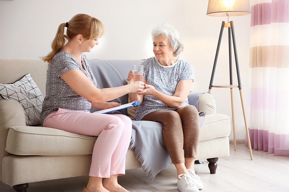 young woman giving a mature woman a glass of water, both women sitting down on a couch