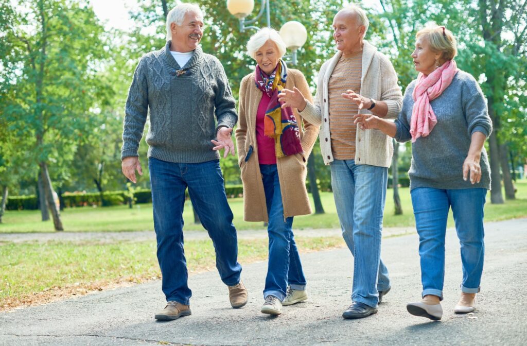A group of four seniors is going for walk in the park and happily chatting on the way enjoying a sunny day.