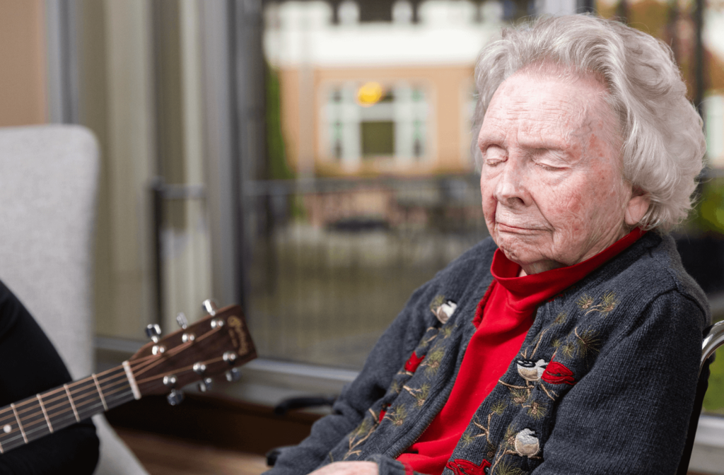 An older adult woman closes her eyes as she listens to a song during a music therapy session