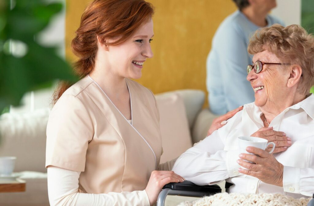 A female caretaker talks to an assisted living resident as she drinks her coffee.