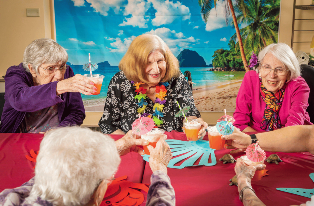 A group of female assisted living residents enjoying fruity drinks together and smiling.