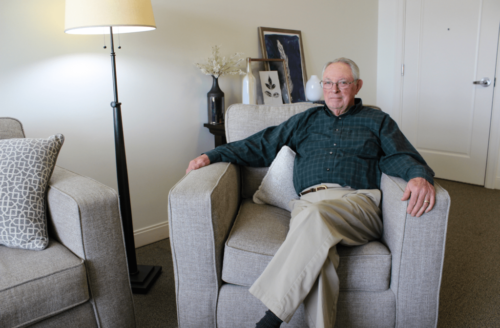 A male senior living resident sitting on a chair in his assisted living apartment