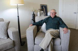 A male senior living resident sitting on a chair in his assisted living apartment
