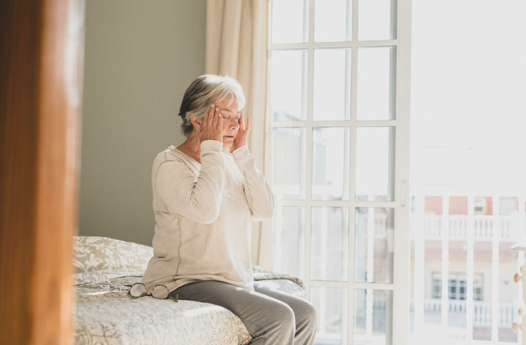 A senior woman sitting at the edge of her bed trying to comfort herself after a dizzy spell