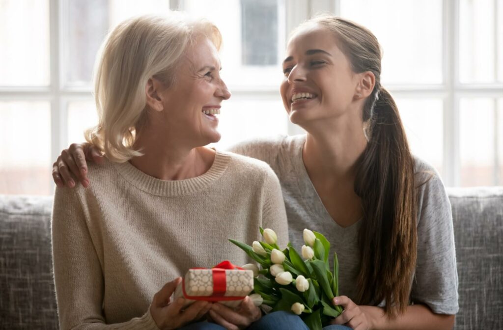 A young woman laughing as she gives her grandmother a gift and white flowers.