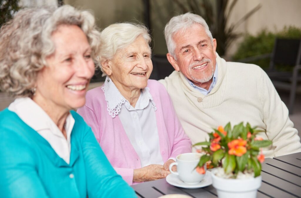 An older man and two older women smile while sitting at a table at a memory care community