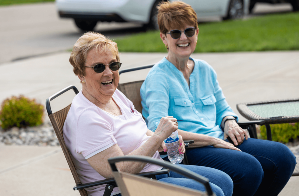 two senior women sit on a bench outside wearing sunglasses