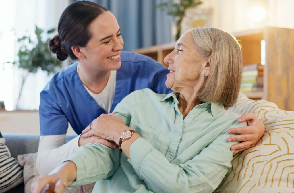 An older adult in a green button-up smiles as their nurse hugs them by the shoulders during a home visit