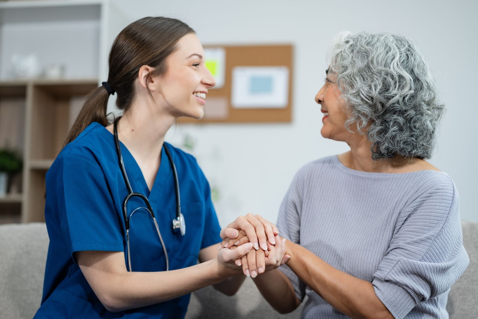 An older person holding hands with their health care aid as they support them in assisted living.