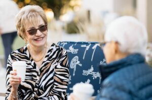 Two older adults holding coffee socialize on the outdoor Plaza at Bethany Village.