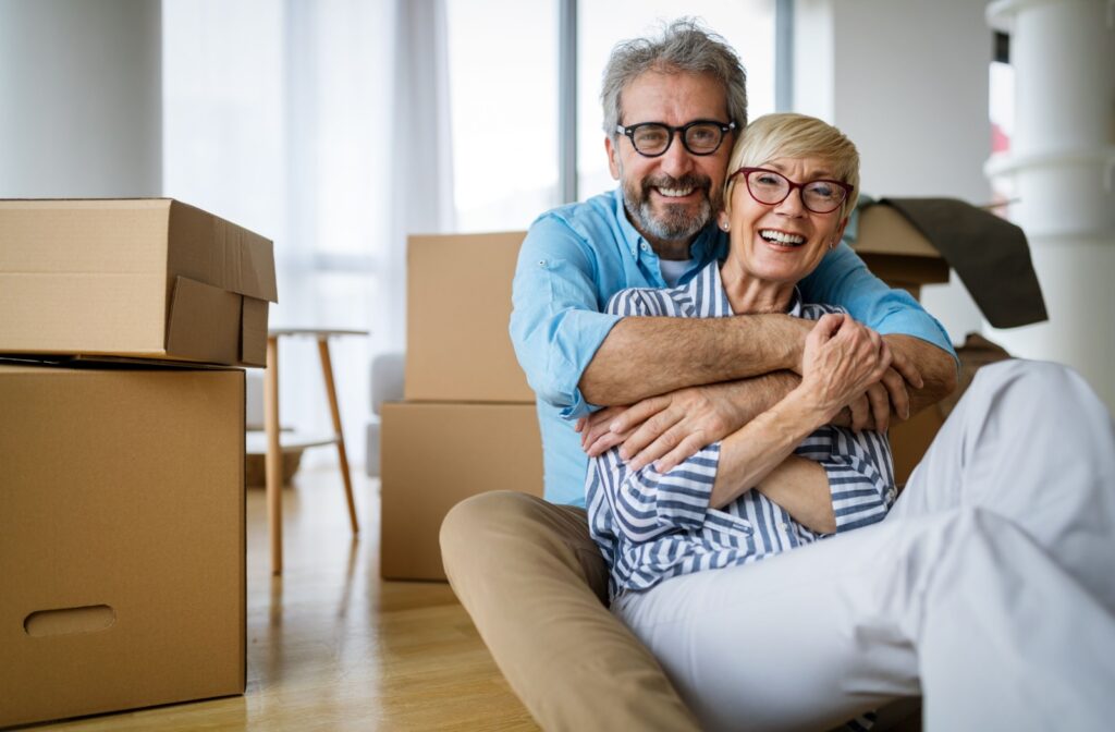 An older couple sits on the floor, cuddling and radiating happiness as they embrace the prospect of moving to an independent living community, anticipating a new chapter filled with shared joy and freedom.