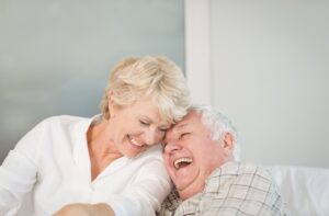 A senior couple laughing while sitting on a couch in an assisted living community.