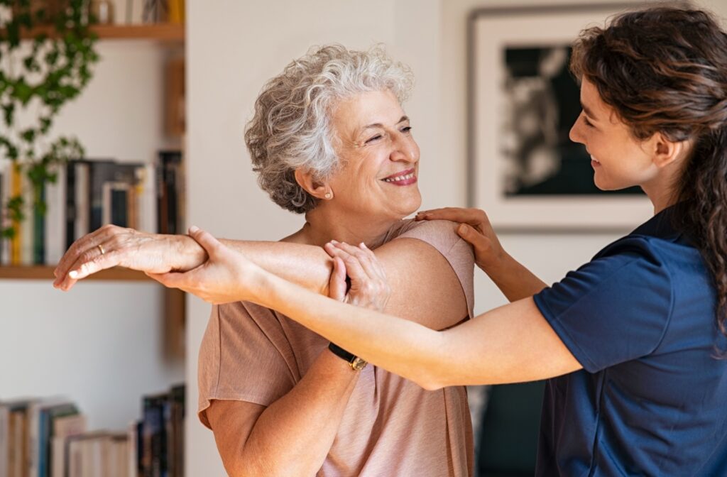 A cheerful older adult is guided through stretches by a rehabilitation therapist.