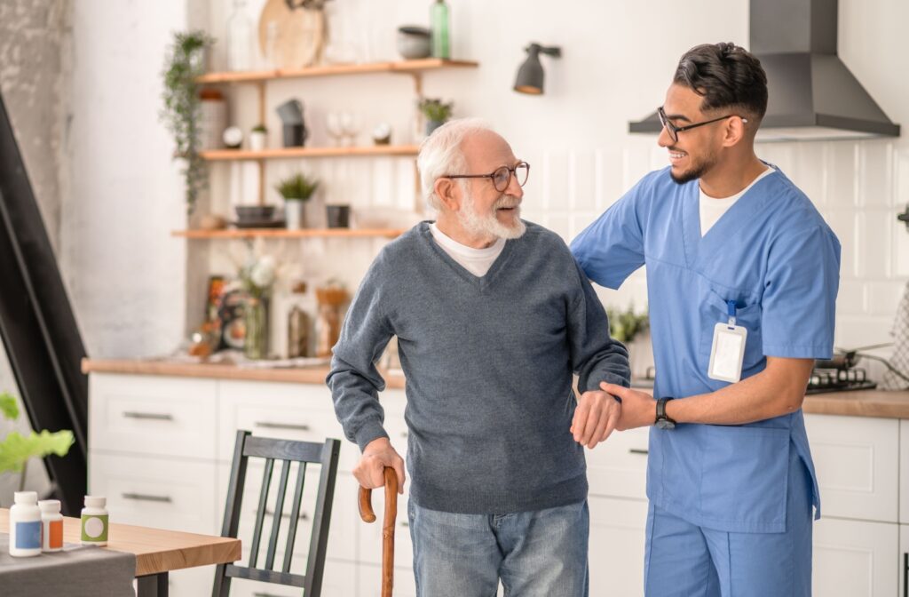 a young male caregiver holds the arm of a senior man in support
