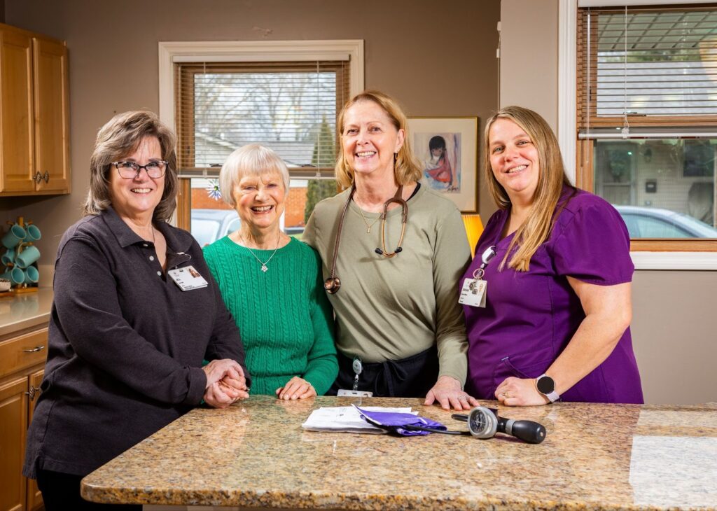 a group of bethany village caregivers stand in a kitchen smiling with a senior woman in her home