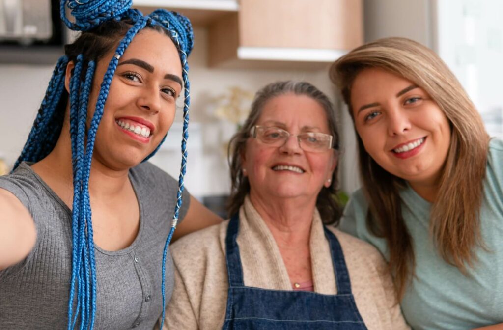 A senior takes a selfie with their adult grandchild and their partner during a visit to their senior living home