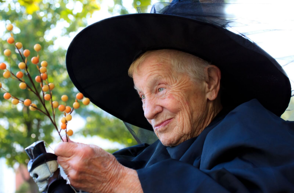 A senior dressed in a witch hat and cloak smiling outdoors celebrating Halloween