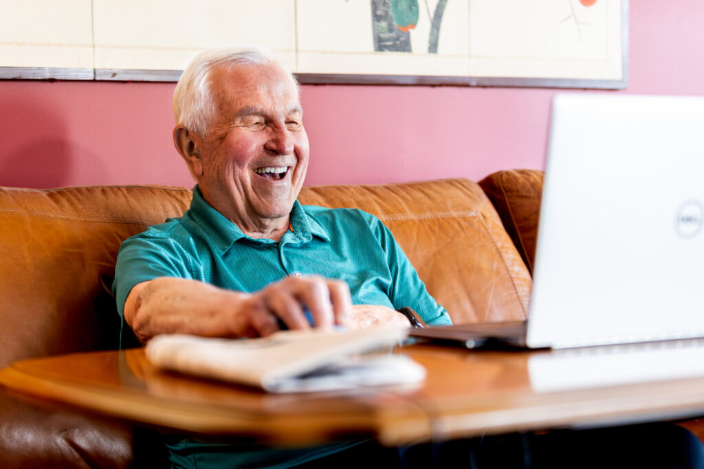 a senior sites at a desk smiling at a laptop