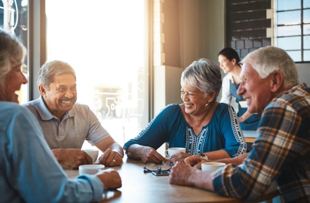 A group of older adults laugh together in a little cafe in their senior living community