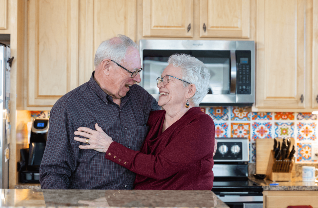 two seniors hugging and smiling in a kitchen